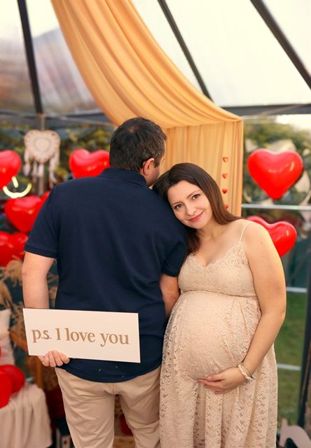 Kobieta w ciąży z partnerem, w dłoniach tabliczka „ps. I love you”