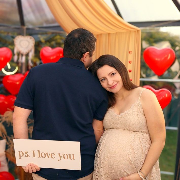 Kobieta w ciąży z partnerem, w dłoniach tabliczka „ps. I love you”