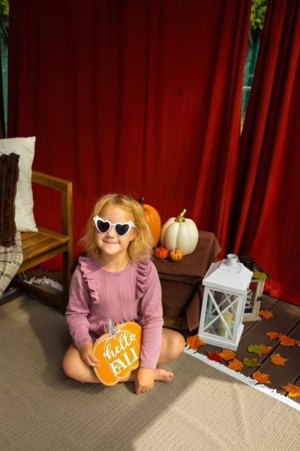 Dziewczynka z tabliczką „hello fall” wśród jesiennych liści