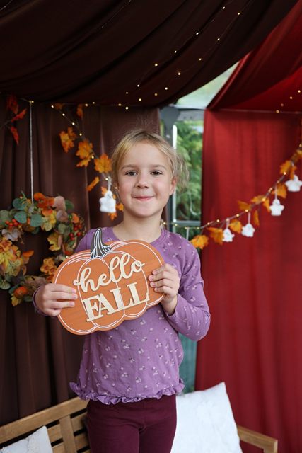 Dziewczynka z tabliczką „hello fall” w kształcie dyni