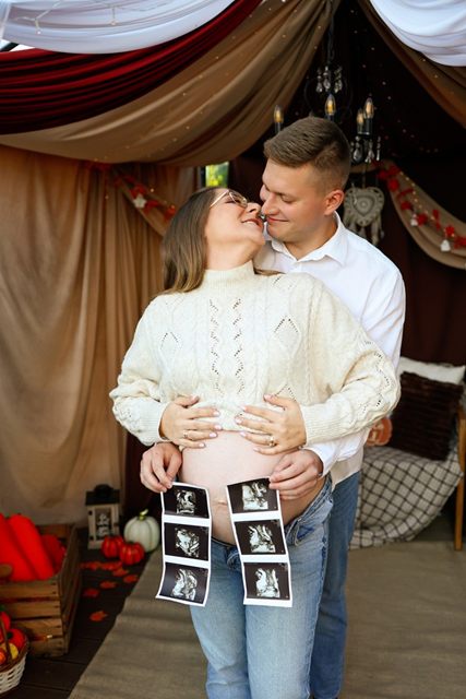 Mężczyzna obejmuje ciężarną partnerkę, przed brzuszkiem paski zdjęć USG
