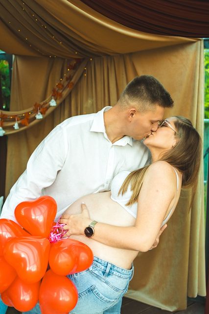 Para w oczekiwaniu całuje się, w dłoni czerwone balony w kształcie serc