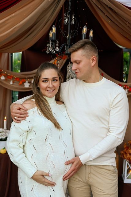 Para w kremowych swetrach obejmuje się z dłońmi na brzuszku
