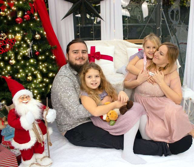 Rodzina z dwiema córkami przy choince, obok figura Mikołaja