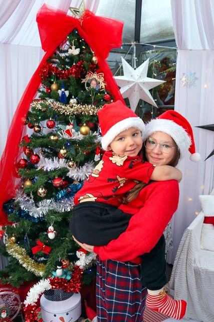 Mama z synkiem w mikołajowych czapkach przy ubranej choince
