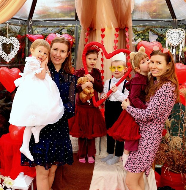 Mama podnosi dziewczynkę w białej sukience, obok rodzeństwo